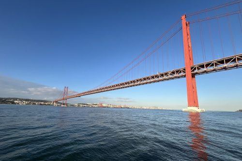 Veleiro navegando no Rio Tejo por baixo da estrutura da Ponte 25 de Abril em Lisboa.